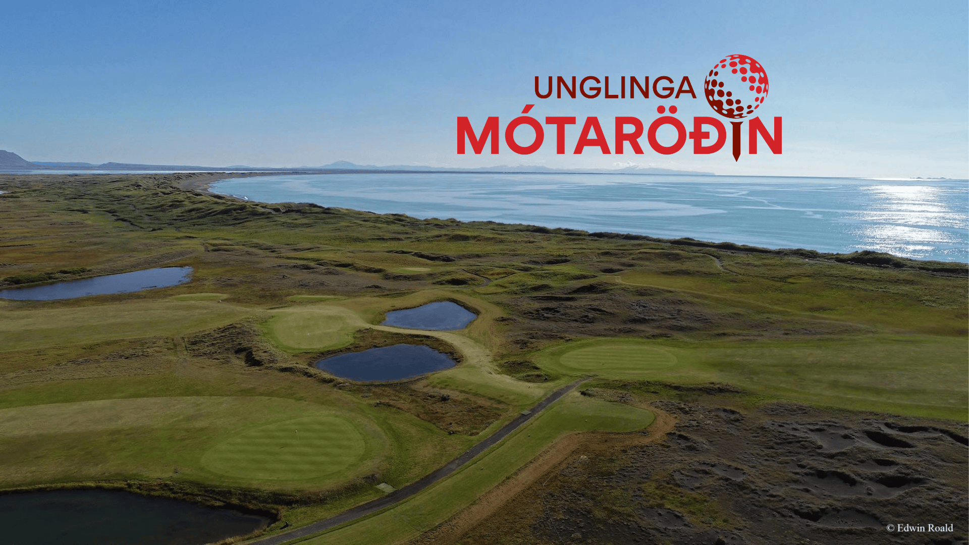 Aerial view of a coastal golf course with greens and bunkers, the sea on the horizon and a red 'UNGLINGA MÓTARÖDIN' logo in the sky.