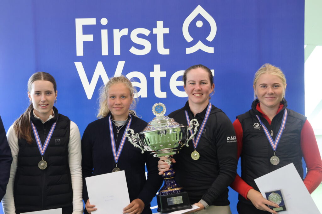 Four young athletes wearing medals pose with a large trophy in front of a blue backdrop that reads 'First Water'.