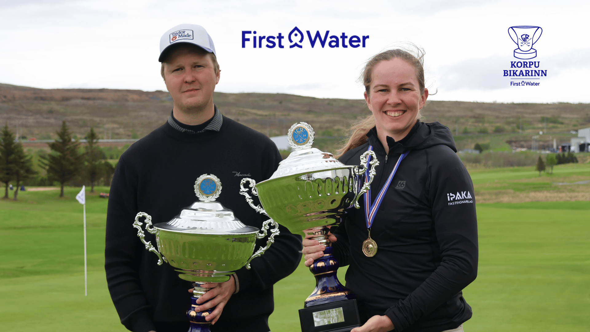 Two athletes on a golf course pose with large trophies, smiles on their faces, First Water logo above and a sponsor crest to the right.
