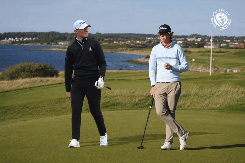 Two men in golf attire walk on a green fairway near a water hazard, each holding a golf club, with a league logo in the skyward corner.