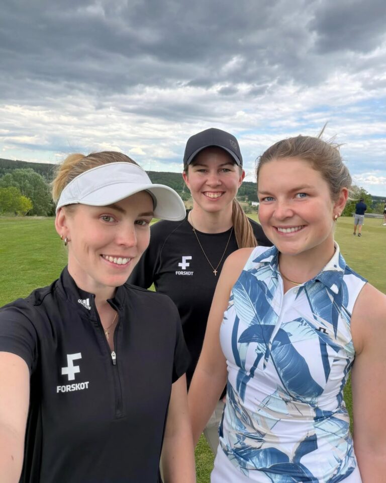 Three women taking a daytime selfie on a grassy field; two wear FORSKOT branded sportswear, one in a white visor and another in a black cap, with a cloudy sky behind them.