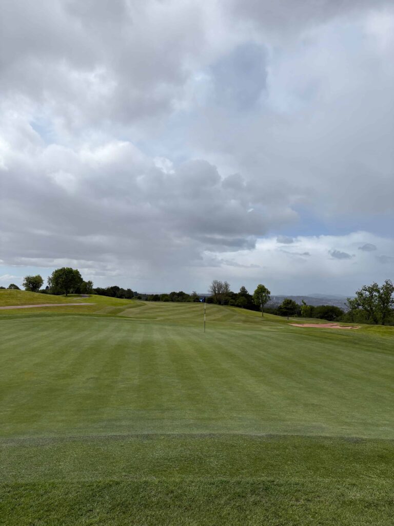 Golf course green with flagstick in the distance under a cloudy sky