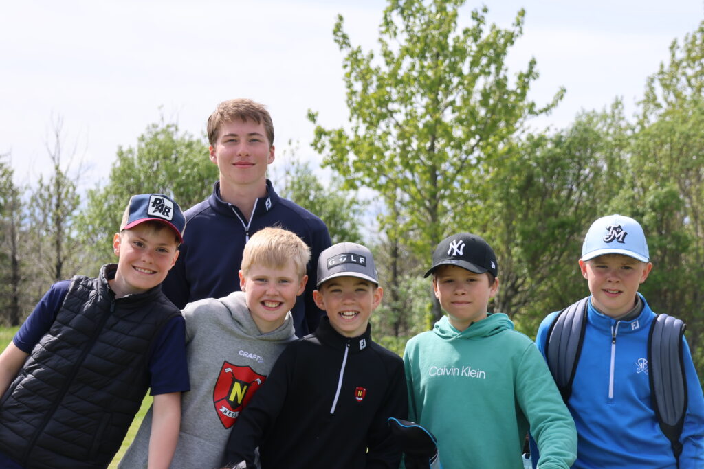 499A0347 - Golfsamband Íslands Group of smiling boys standing close together outdoors on a sunny day with trees in the background.