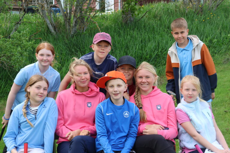 Group of smiling children wearing colorful jackets posing for a photo outdoors in a grassy area.