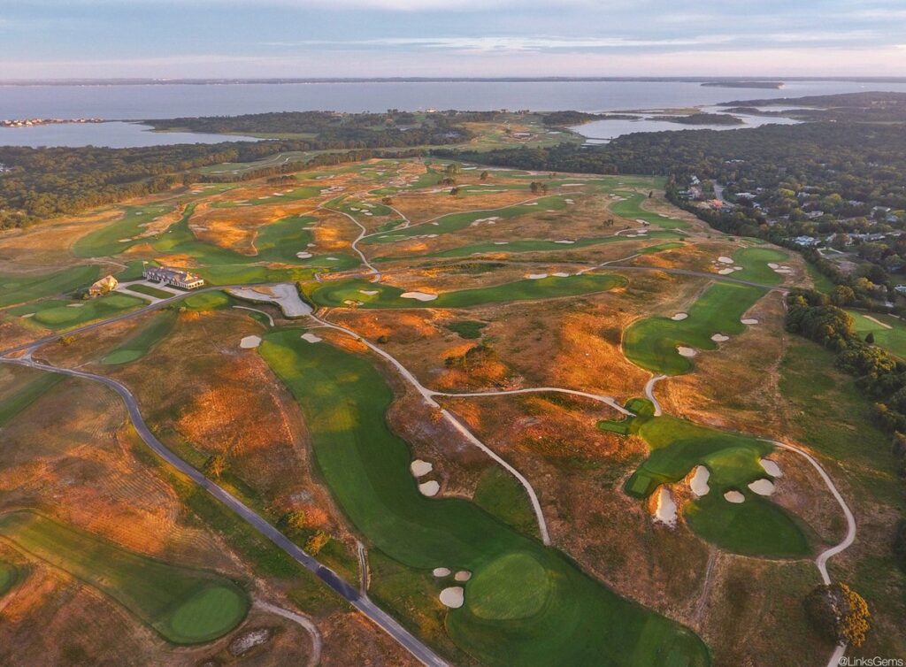 Aerial view of a coastal golf course with winding fairways, sand traps, and a clubhouse on the left.