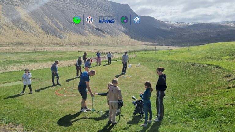 Group of adults and children playing golf on a grassy field with mountains in the background; equipment and colorful rings laid out on the ground, weather sunny and clear.