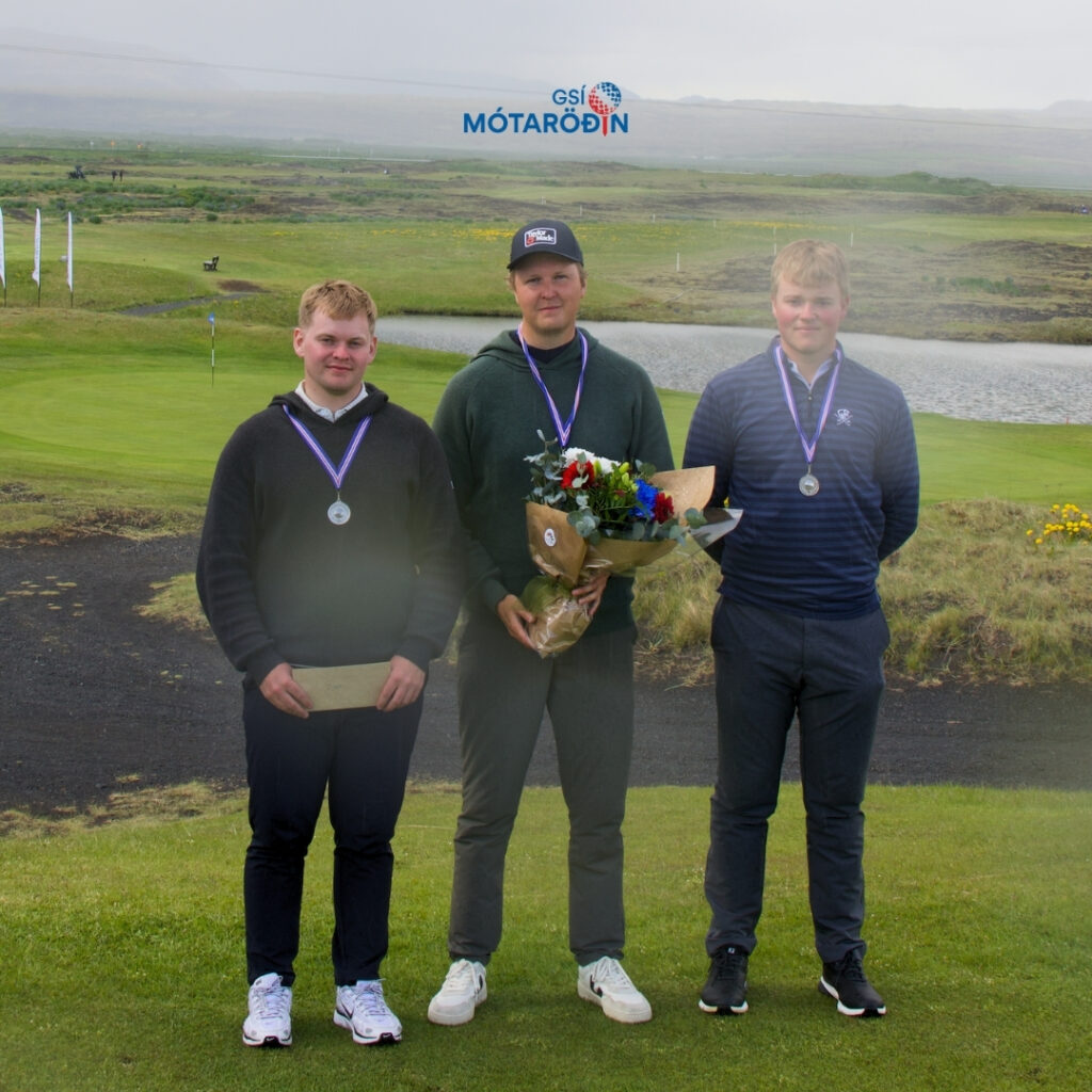 Heading - 2026-06-07T180139958 - Golfsamband Íslands Three young men stand on a golf course podium wearing medals; one holds a bouquet of flowers and an envelope.