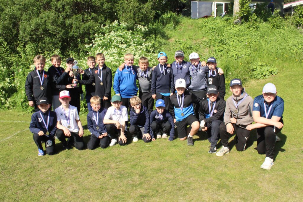IMG_2876 1 - Golfsamband Íslands Young boys posing outdoors with medals and a trophy after a sports event on a grassy field.