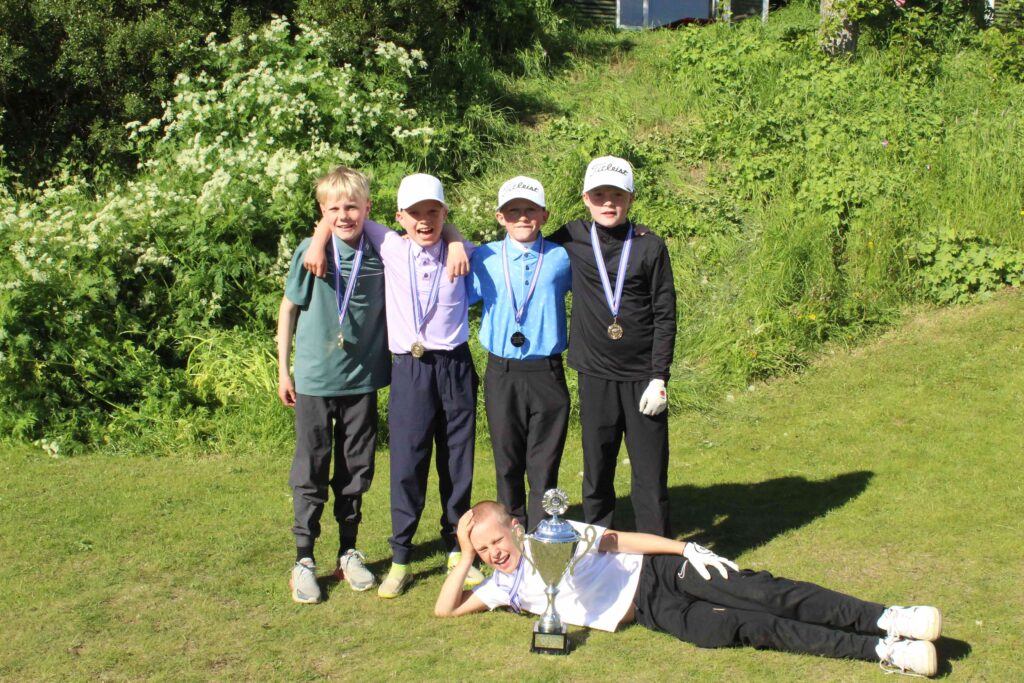 IMG_2881 1 - Golfsamband Íslands Group of young golfers standing with medals, posing outdoors beside a large trophy on the grass.