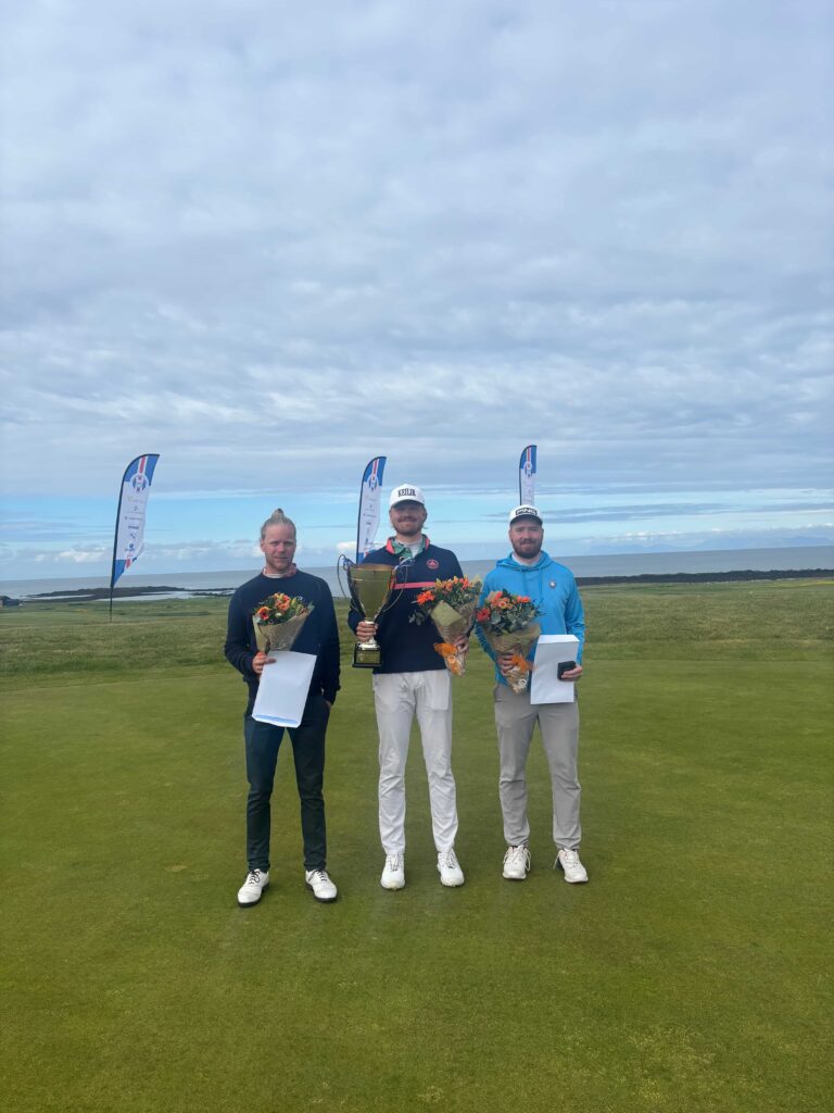 IMG_2898 - Golfsamband Íslands Three men stand on a golf course holding a trophy and bouquets, celebrating a win.