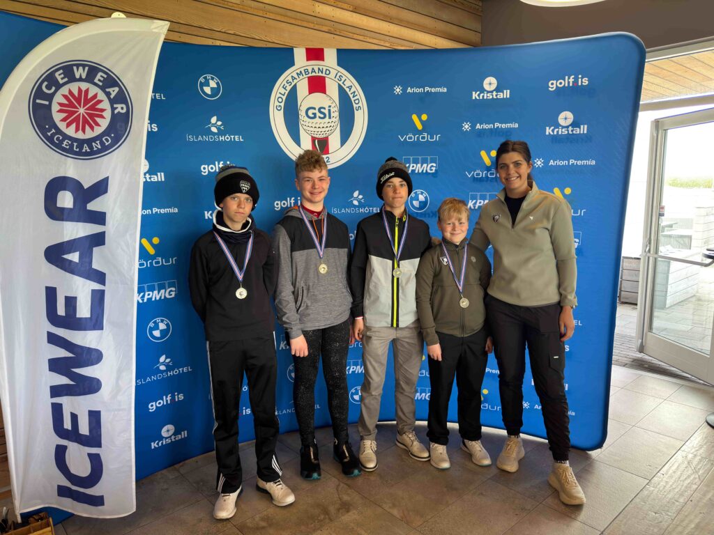 IMG_8939 1 - Golfsamband Íslands Five young golfers with medals stand in front of a blue event backdrop featuring Golf.is, Kristall and Arion Premia logos, with a tall white Iceland flag on the left.