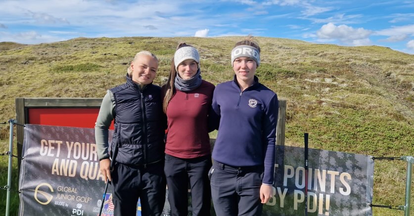 SnapInstato_719609596_18377398063206695_3822381300555027964_n - Golfsamband Íslands Three young women pose together outdoors on a sunny day, smiling, in athletic jackets and headbands, with golf banners in the background.