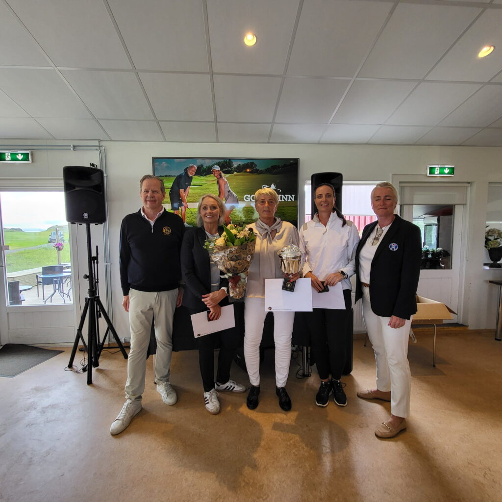 1000029115 1 - Golfsamband Íslands Six people posing indoors with certificates and a bouquet, wood floor and a golf-themed poster in the background.