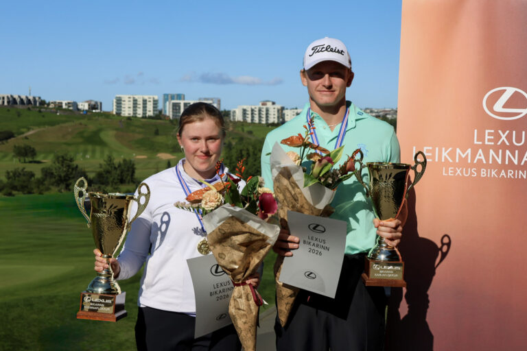 Two young athletes stand on a podium, holding large trophies and bouquets, smiling with a Lexus banner in the background.