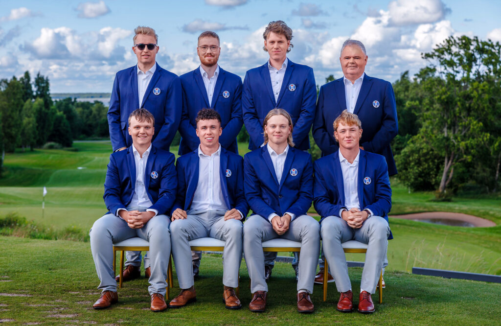 ETAC2026-26 - Golfsamband Íslands Eight men in matching blue blazers pose for a team photo on a golf course, arranged in two rows (four standing, four seated).
