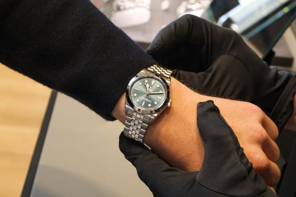 Close-up of a metal wristwatch on a man's left wrist with a teal dial and stainless steel bracelet?