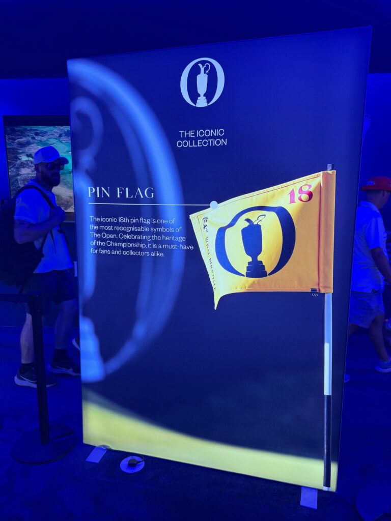 IMG_5231 - Golfsamband Íslands Blue exhibition banner reading'THE ICONIC COLLECTION' with a white trophy logo and a yellow pin-flag graphic titled 'PIN FLAG' on the right side, against a curved light pattern.