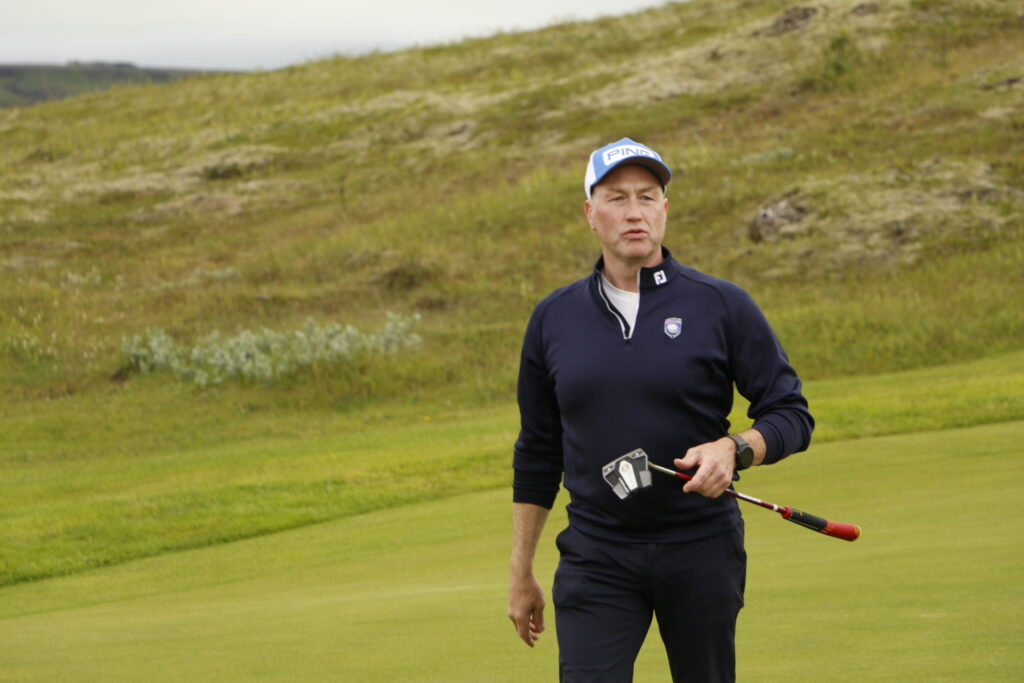 _MG_0951 - Golfsamband Íslands Man in a navy pullover and PING cap stands on a grassy field, holding a golf club/training rod outdoors.