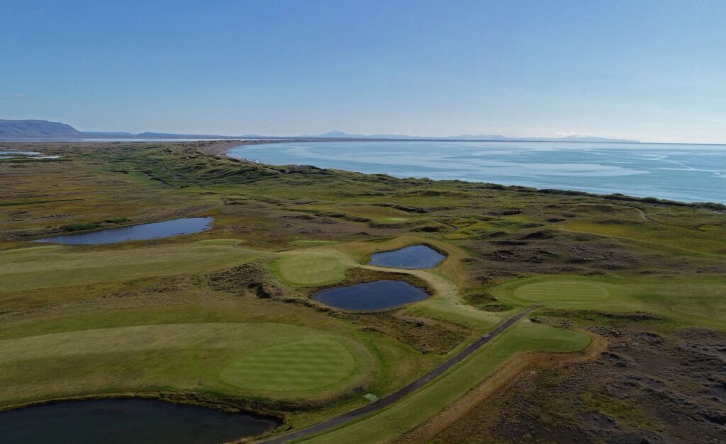 Aerial view of a coastal golf course with green fairways, ponds, and the blue ocean in the distance.