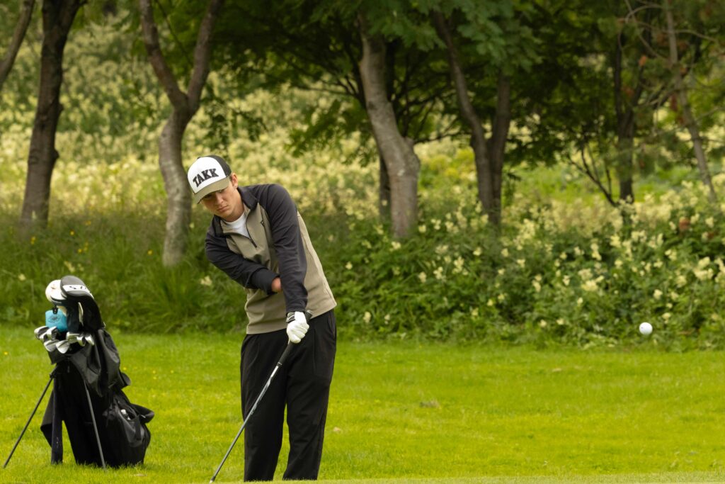 6-499A5143 - Golfsamband Íslands Golfer preparing to swing on a lush green golf course with a bag of clubs nearby.