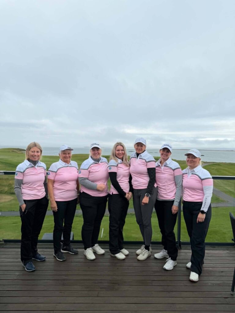 775656489_1451687656768168_930183927339662692_n - Golfsamband Íslands Group of women golfers posing together on a wooden deck, wearing pink and white tops and caps, with a grassy course in the background.