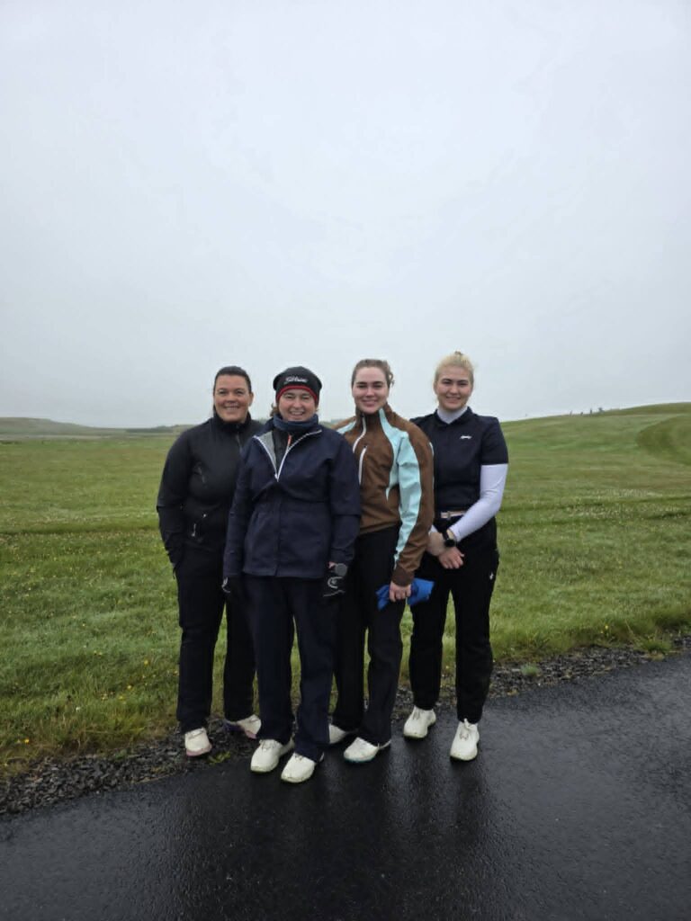 777478474_1451687520101515_9138118399536325785_n - Golfsamband Íslands Four people stand together on a grassy field under a cloudy sky, wearing jackets and athletic gear for an outdoor outing.