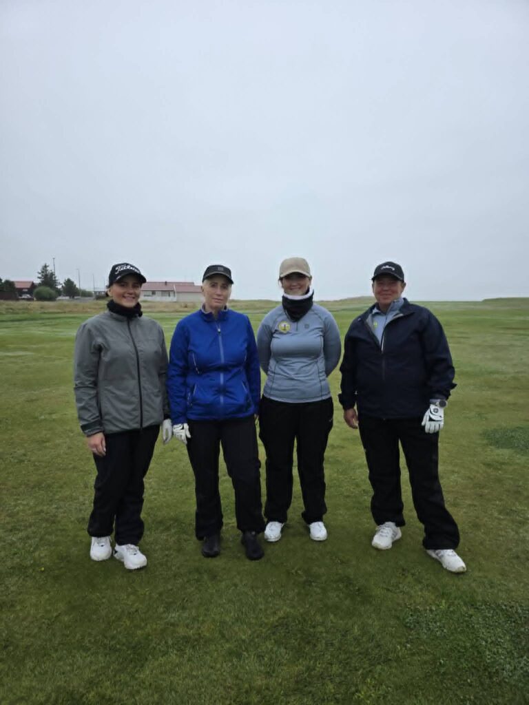 777951606_1451687440101523_7141146037891387187_n - Golfsamband Íslands Four people standing side by side on a grassy golf course under a cloudy sky, wearing jackets and caps.