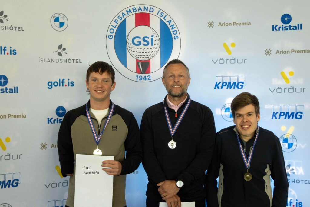8-499A5195 - Golfsamband Íslands Three men with medals posing on a podium after a competition, holding certificates in front of a sponsor backdrop.