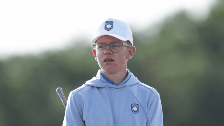 Young person wearing a white cap with a Team Iceland logo and a light blue hoodie, holding a hockey stick outdoors.