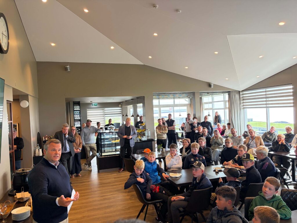 IMG_8651 - Golfsamband Íslands Crowd gathered in a bright cafe-style room, with people seated and standing as a speaker addresses them from the left.