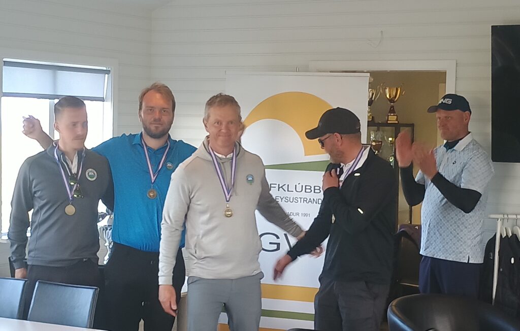 a5772a3b-c71f-4085-97b9-8a6c3902111b~1 - Golfsamband Íslands Five men wearing medals pose for a photo at an indoor awards event, standing in front of a banner and windowed wall.