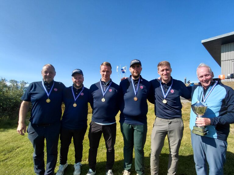 Six men in matching navy polo shirts pose outdoors with medals around their necks and a trophy, celebrating a win.